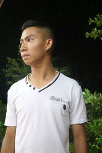 Young man looking away while standing against plants