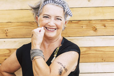 Portrait of smiling senior woman flexing muscles against wooden wall