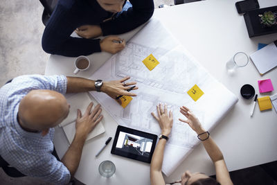 Overhead view of architects discussing over blueprints and digital tablet at creative office