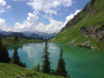 Scenic view of lake by mountain against cloudy sky