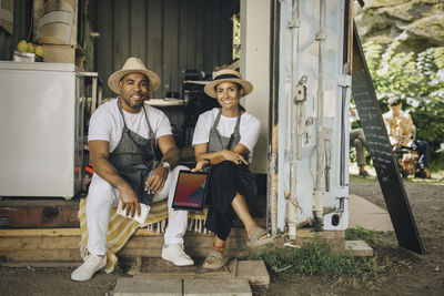 Portrait of smiling male and female colleagues sitting at doorway of food truck