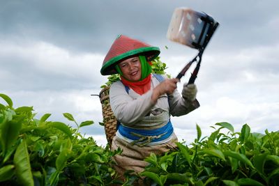 Midsection of woman holding hat on field against sky