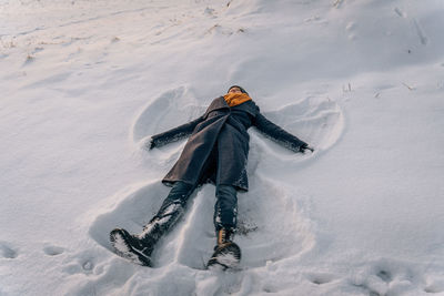 A woman lies in the snow in the shape of a snow angel in winter