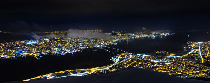 Illuminated city by sea against sky at night