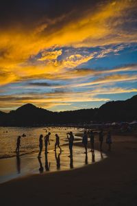 Silhouette people on beach against dramatic sky