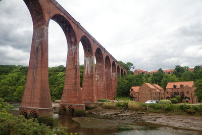 Arch bridge over river by old building against sky