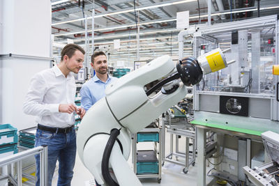 Two men looking at assembly robot in factory shop floor