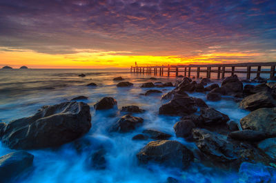 Rocks at beach against cloudy sky during sunset