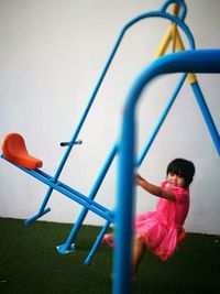 Girl playing on seesaw at playground against wall