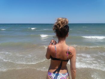 Rear view of young woman standing at beach against sky