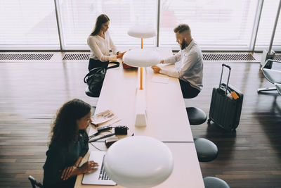 High angle view of colleagues waiting while using technologies at airport departure area