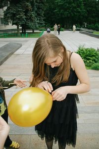 Smiling girl tying yellow balloon at park