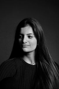 Thoughtful young woman with long hair standing against black background