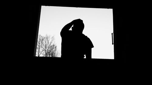 Low angle view of silhouette man standing against window