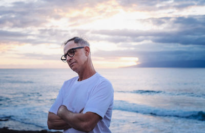 Portrait of young man looking away against sea during sunset