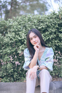 Portrait of young woman sitting against plants in park