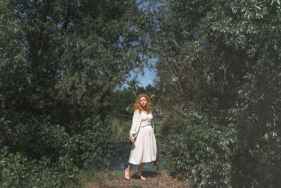 Portrait of woman standing by plants against trees