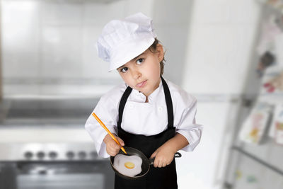 Portrait of girl in chef uniform preparing fried egg in kitchen