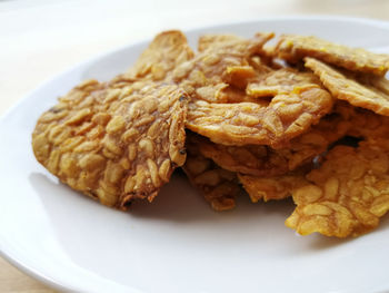 Fried tempeh in a white plate on the wooden surface.