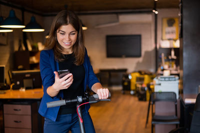 Businesswoman with electric scooter using smart phone at office