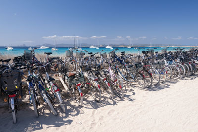 Bicycles parked on a beach on the island of formentera. in the background blue sky, sailboats moored