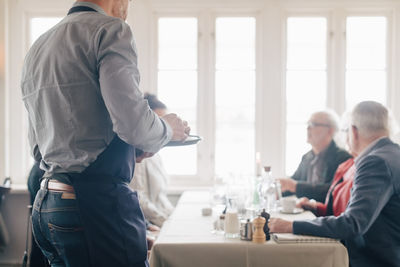 Midsection of owner standing by table while male and female sitting in restaurant