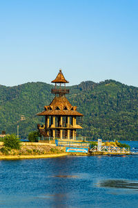 Built structure by lake against clear blue sky