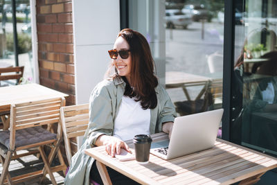 Adult smiling brunette business woman forty years in stylish shirt working on laptop in cafe  