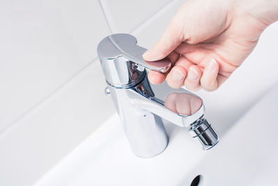Close-up of person using faucet in bathroom