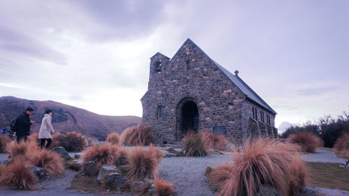 People walking towards old church against sky at sunset