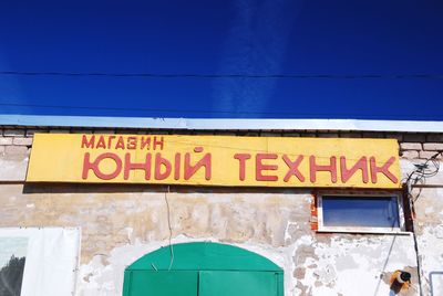 Low angle view of text on wall against blue sky