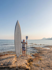 Sporty mature man in sunglasses with big surfboard in water on seaside looking away in alicante spain