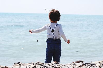 Rear view of boy standing on stones by sea against sky