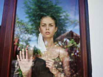 Portrait of young woman looking through window