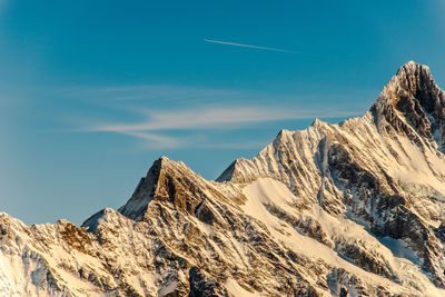 Low angle view of snowcapped mountains against blue sky