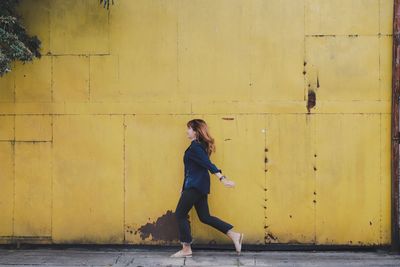 Side view full length of woman walking by yellow wall