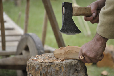 Midsection of carpenter cutting wood on tree stump