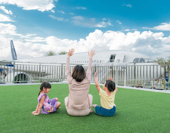 The back view of happy family mother woman and baby kids, raising arms fun greeting the plane.