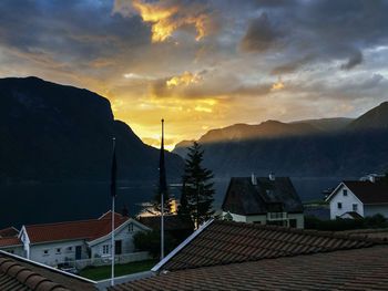 Houses by mountains against cloudy sky during sunset