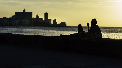 Silhouette people sitting on beach against sky during sunset