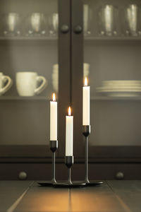 Tree burning white candles in holders over black dining table - vertical