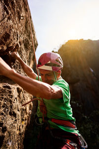 From below side view unrecognizable active fit senior man climbing on rocky cliff