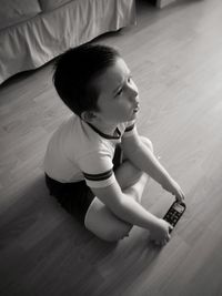 Cute boy with remote control looking away while sitting on floor