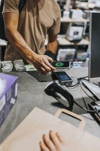 Midsection of male customer scanning credit card reader through smart phone at checkout in electronics store