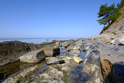 Rocks by sea against clear blue sky