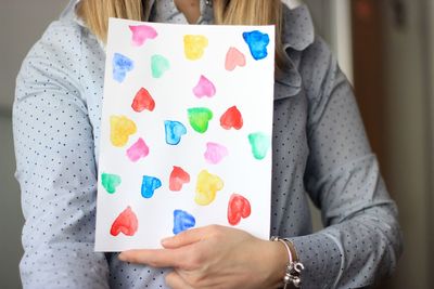 Midsection of woman holding heart shape painting at home