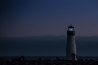Lighthouse by sea against sky at sunset