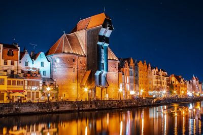 Reflection of illuminated buildings in canal against sky at night