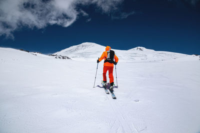 A young sportsman skier in an orange suit climbs a ski tour on a snow-covered slope to mount elbrus