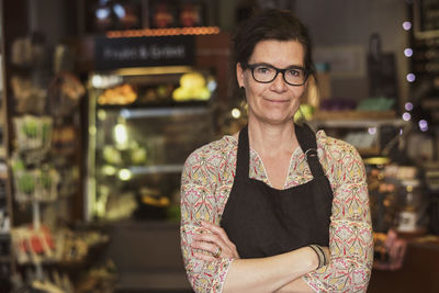 Portrait of smiling owner standing with arms crossed at store